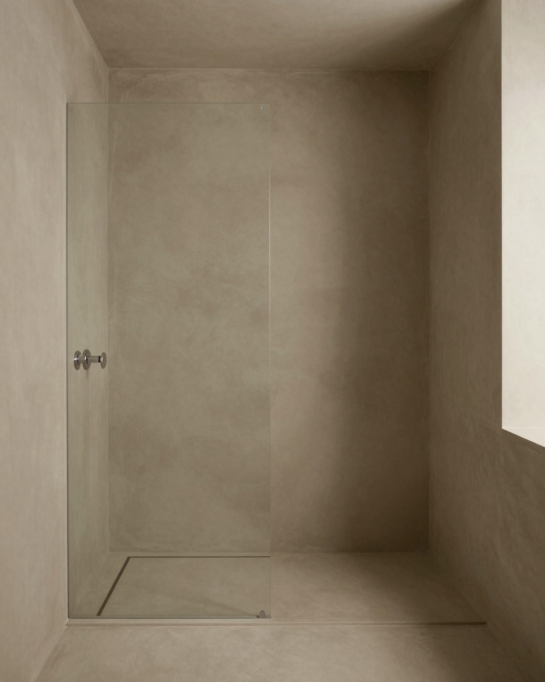 Illustration: a microcement shower and bathroom in warm greige, seamless walls and floor with no grout lines, a linear drain