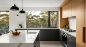 A modern open-plan kitchen in a Canberra home, featuring a large Calacatta marble island, dual-tone charcoal and oak cabinetry, and a window overlooking an Australian bush setting in morning light.